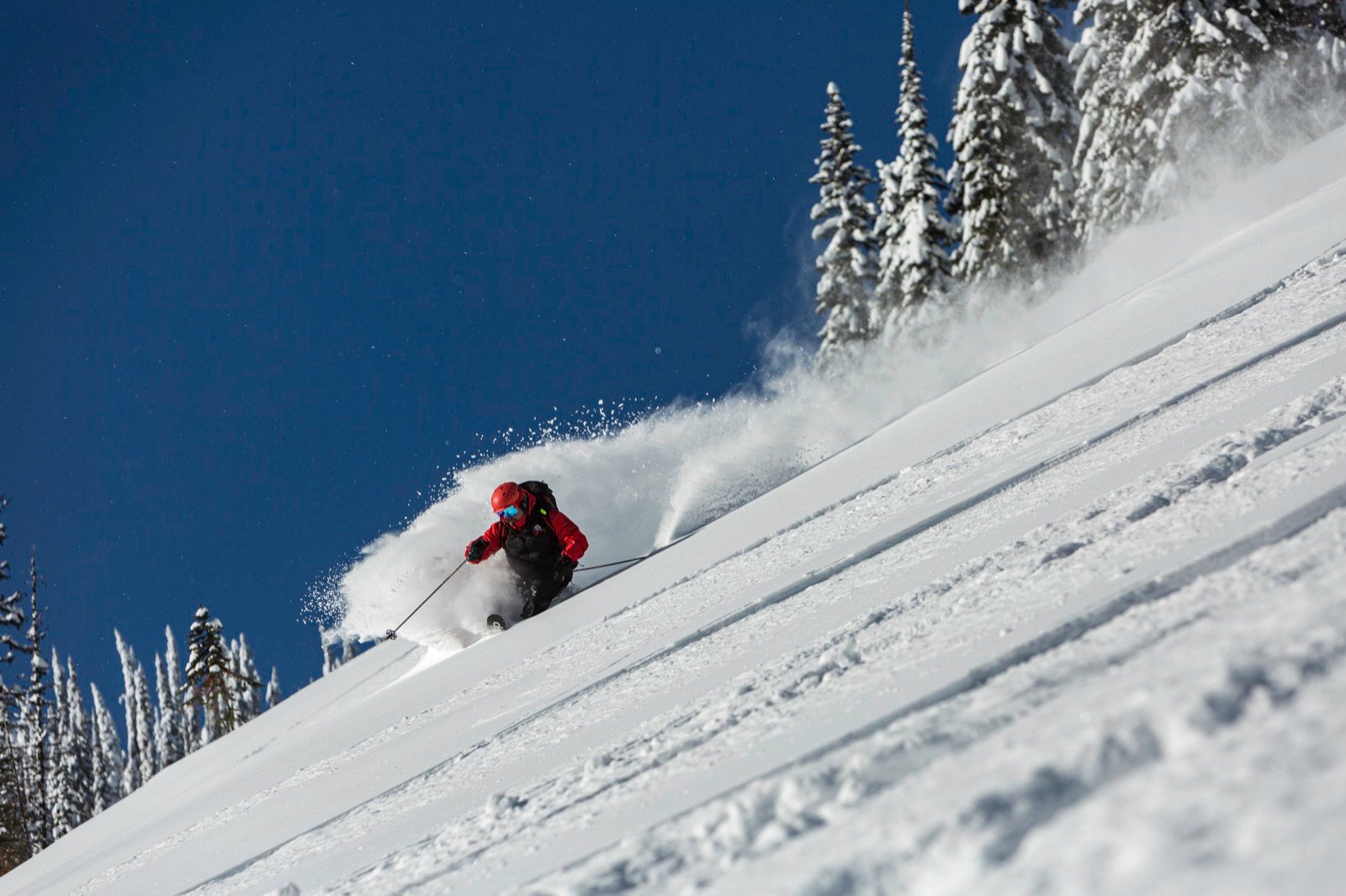 Snowboarder kicking up a spray of powder down a steep slope, Keefer Lake Lodge