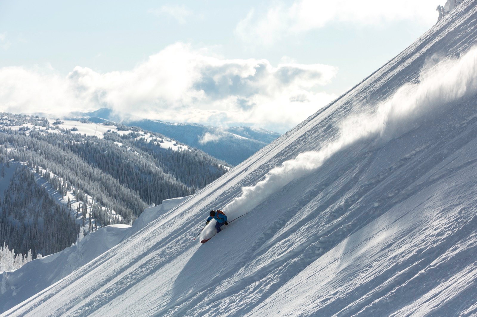 Snowboarder dropping into a steep powder run at Keefer Lake Lodge, BC