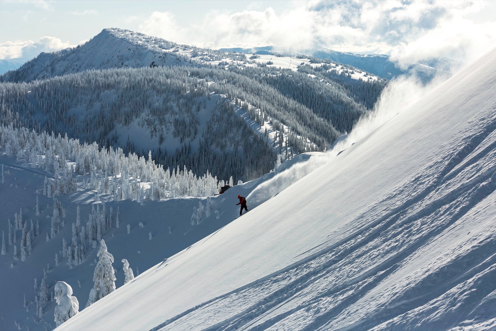 Skier making a deep powder turn above the treeline at Keefer Lake Lodge, BC