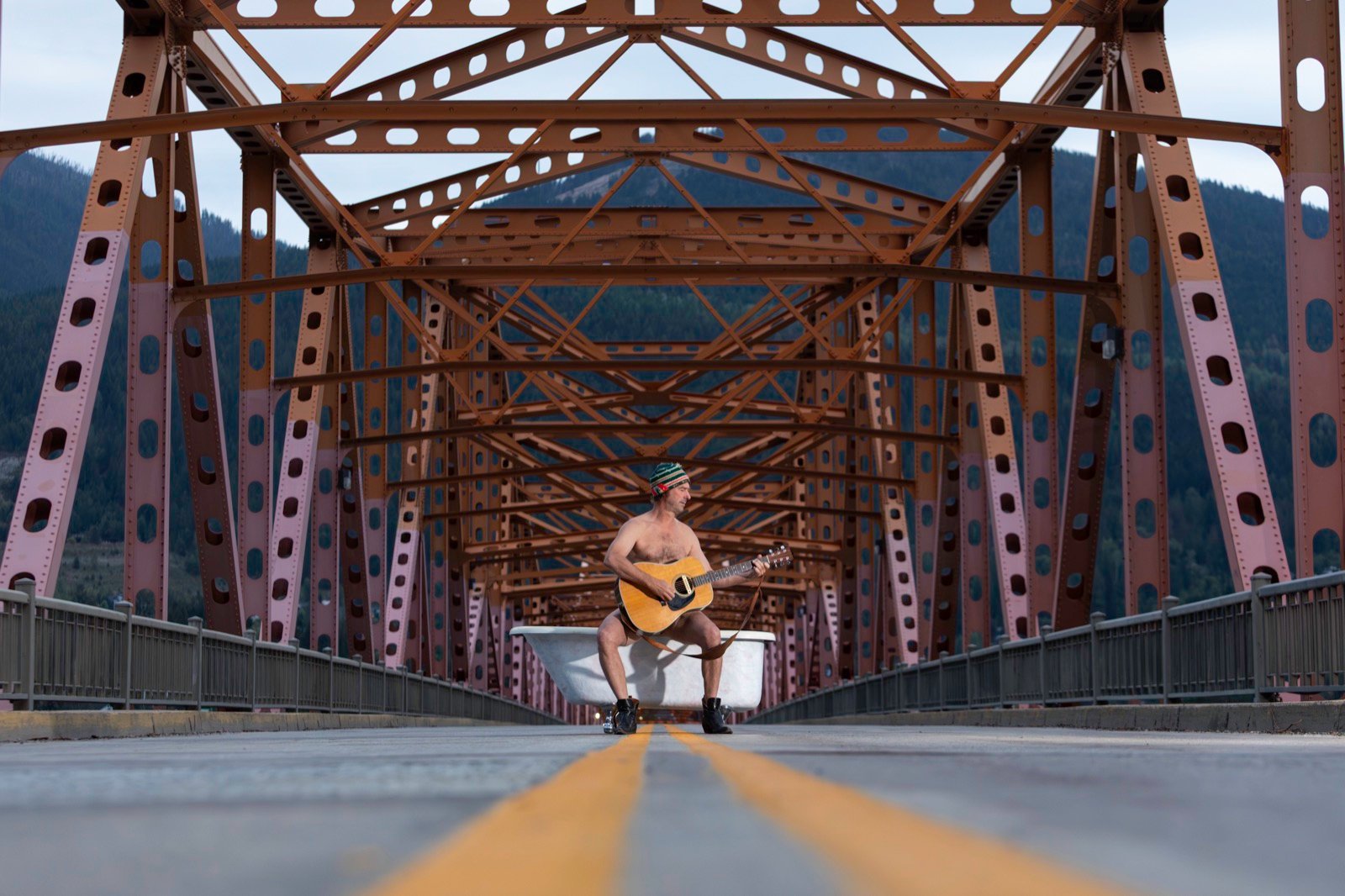 A model playing guitar beside a bathtub on an old steel bridge, Men in Tubs calendar