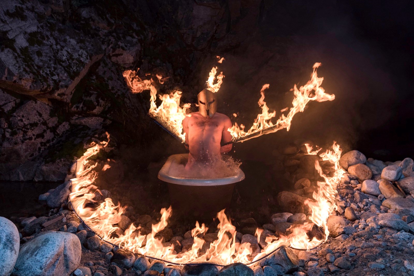 A bathtub encircled by fire at night, Men in Tubs calendar